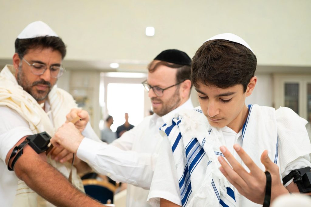 אב ובן בטקס הנחת תפילין בבית כנסת, רגע של מסורת.