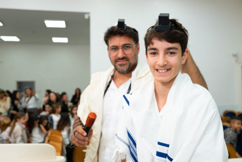 פורטרט נער בר מצווה עם תפילין מחייך בבית כנסת.