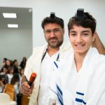 פורטרט נער בר מצווה עם תפילין מחייך בבית כנסת.