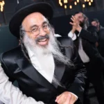 רב מחייך בריקודים בחתונה דתית, לבוש כובע וחליפה שחורה, צילום אירועים מקצועי.