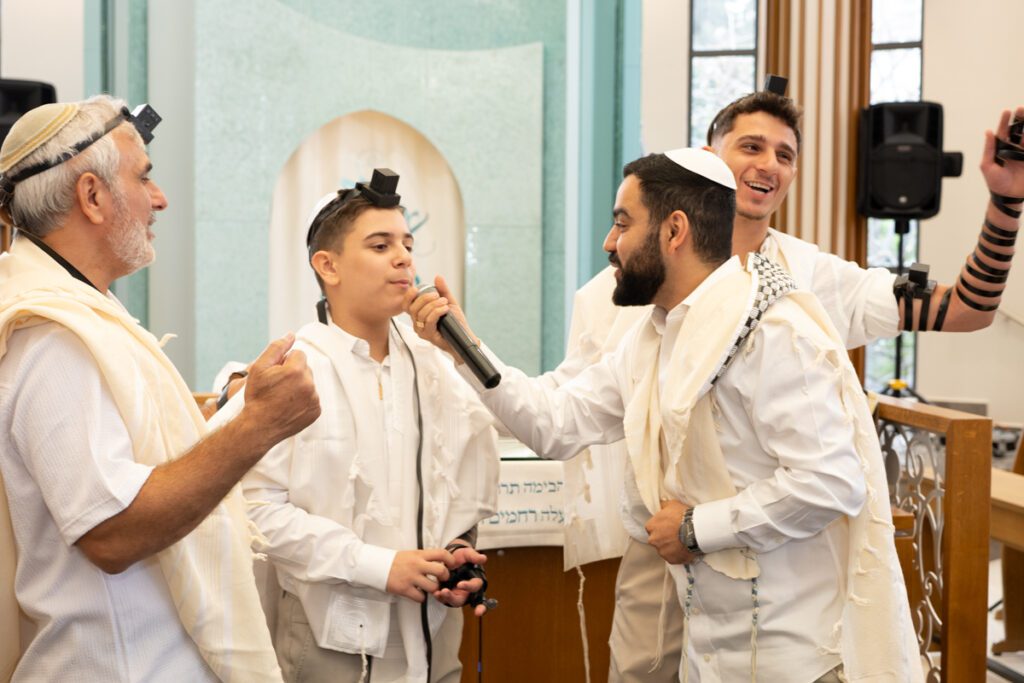 צלם לעליה לתורה בגבעת שמואל, נער בר מצווה שר במיקרופון עם תפילין וטלית