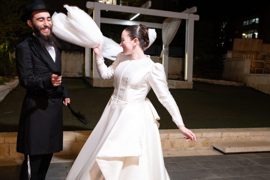 חתן וכלה רוקדים עם אבנט ומחייכים מאושר בחוץ