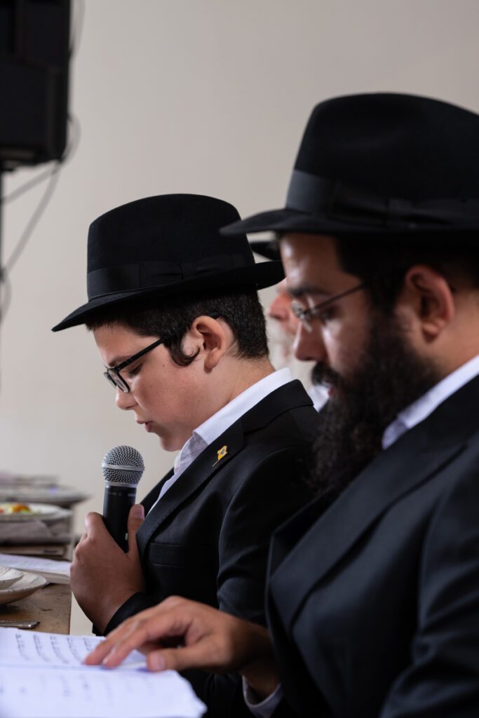 בחור ישיבה צעיר נואם עם מיקרופון בחגיגת בר מצווה חסידית