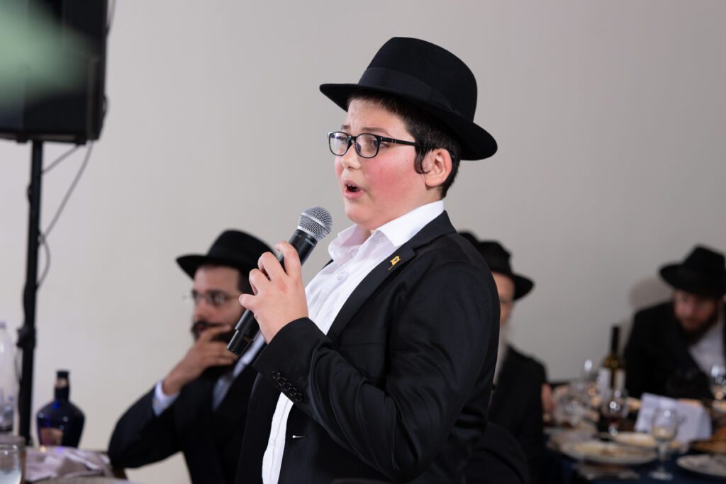חתן בר מצווה צעיר שר עם מיקרופון בחגיגת בר מצווה מלאת שמחה