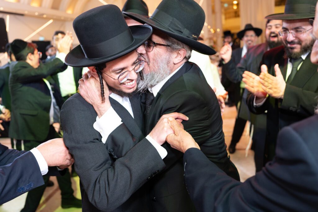 שמחת חתונה חרדית מתפרצת, גברים חרדים רוקדים ומחבקים זה את זה באולם אירועים, צלם אירועים חרדי.