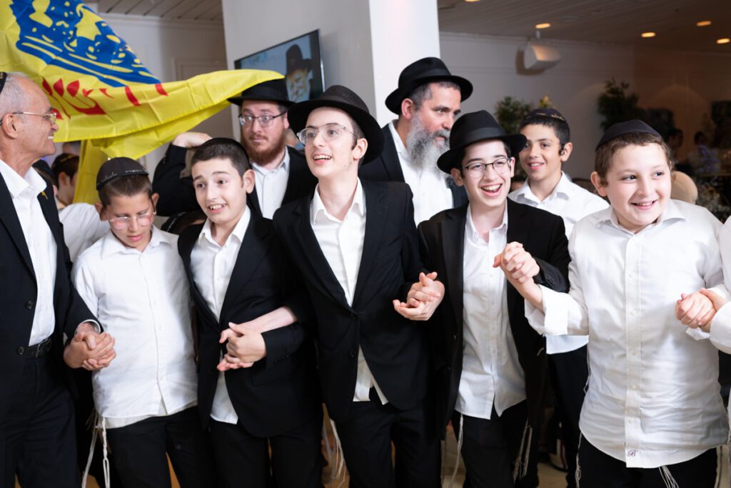 קבוצת ילדים חסידים מחויכים רוקדים עם דגל חב"ד בבר מצווה