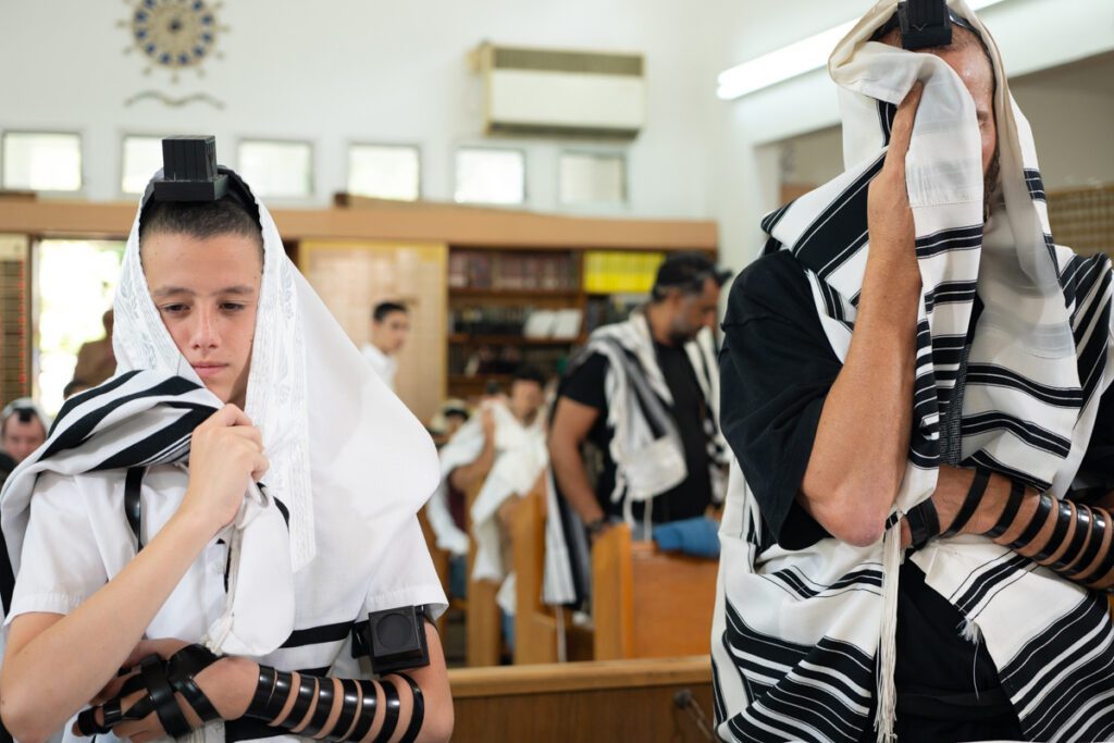 נער בר מצווה מניח תפילין ומתעטף בטלית לצד אביו בבית כנסת בתל אביב