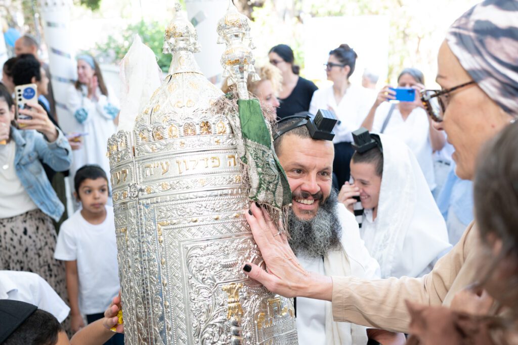 גבר מחזיק ספר תורה מפואר במהלך חגיגת עלייה לתורה בבית כנסת בתל אביב