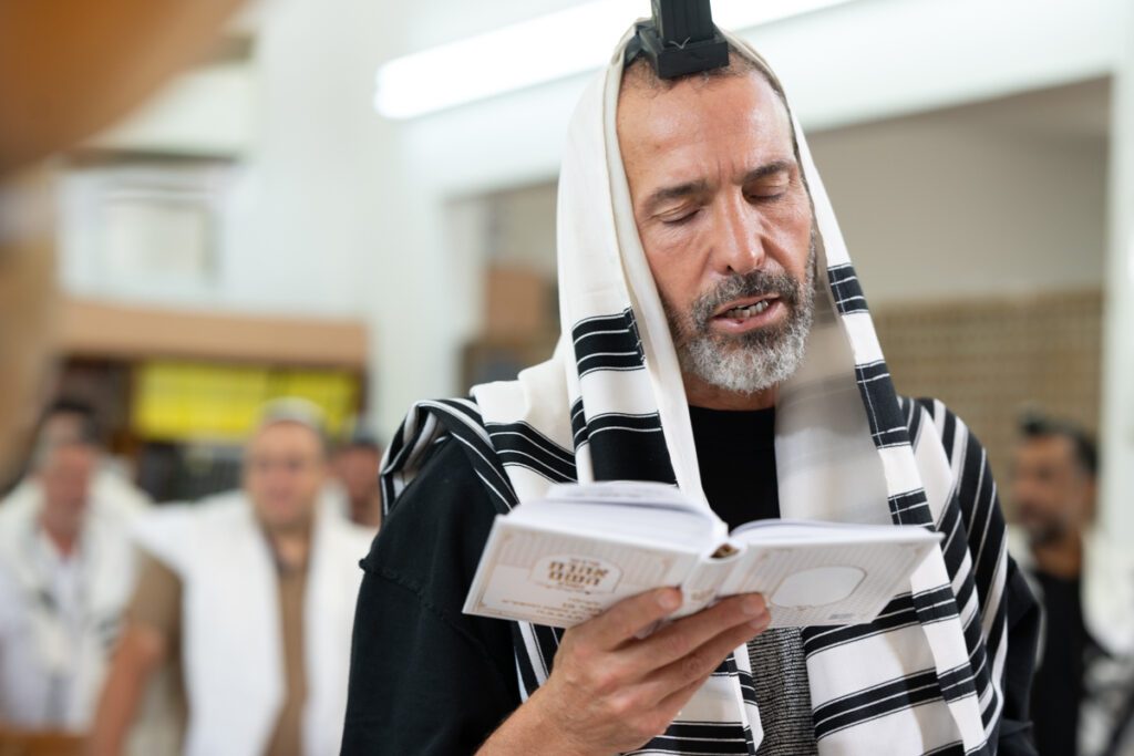 אב מתפלל בדבקות עם טלית ותפילין במהלך עלייה לתורה של בנו בתל אביב