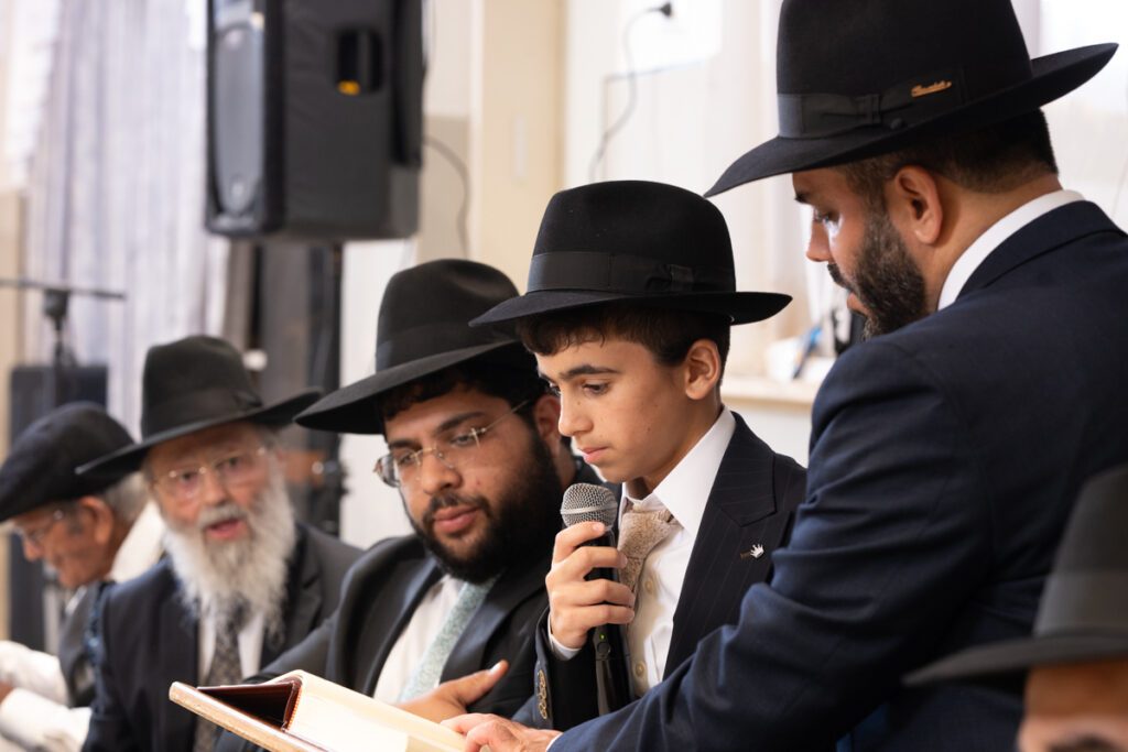 חתן בר מצווה דתי קורא את הדרשה במיקרופון לצד אביו באלעד