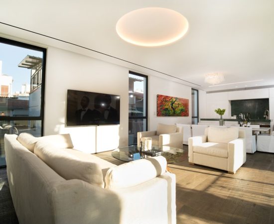 עיצוב סלון מודרני עם ריהוט לבן מינימליסטי, חלונות רחבים הפונים לנוף עירוני, ושילוב של אמנות צבעונית, היוצרים חלל חי ומזמין עם זרימה טבעית של אור