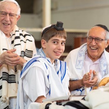 חיוך של נער בר מצווה לצד סבו ובני משפחה, רגע של שמחה וגאווה בסיום קריאה בתורה. צילום שמנציח אהבה משפחתית וחגיגת מסורת.