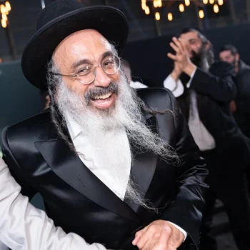 רב מחייך בריקודים בחתונה דתית, לבוש כובע וחליפה שחורה, צילום אירועים מקצועי.