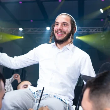 חתן דתי נישא על כיסא במהלך ריקודים בחתונה, תאורת אירועים צבעונית ברקע, צלם חתונות בפתח תקווה.